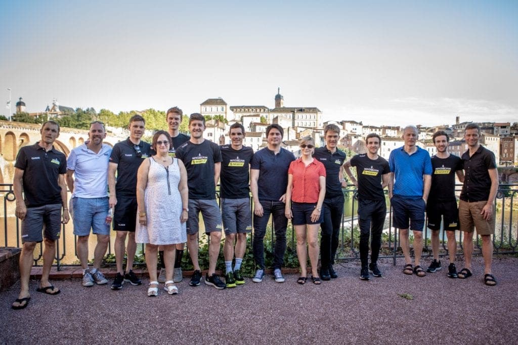 Group photo with cycling team members and guests in front of a bridge.