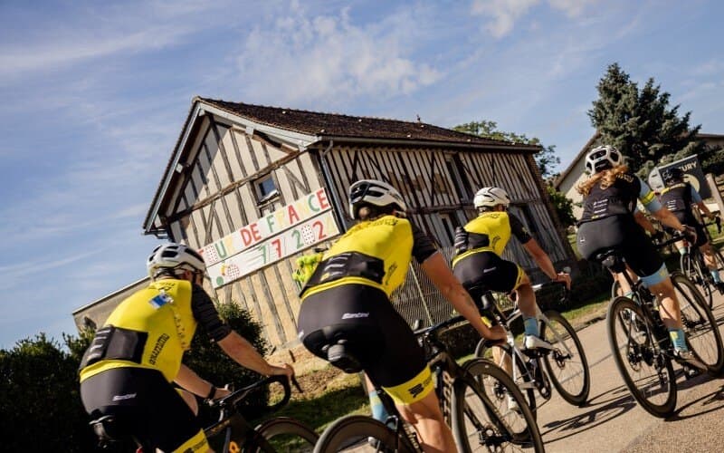 Cyclists in Mummu Cycling kit ride past a building