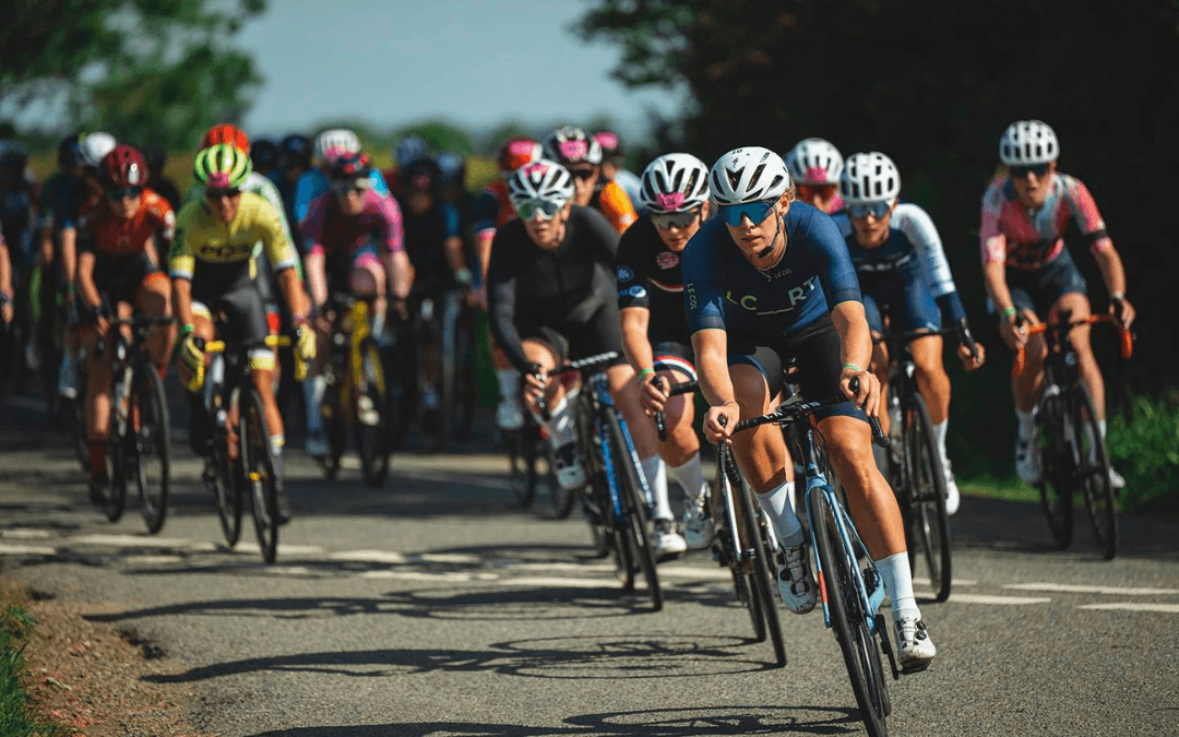 A group of cyclists, including a lead rider in blue and black kit, racing at the UCI Gran Fondo World Championships 2025 on a sunny day.