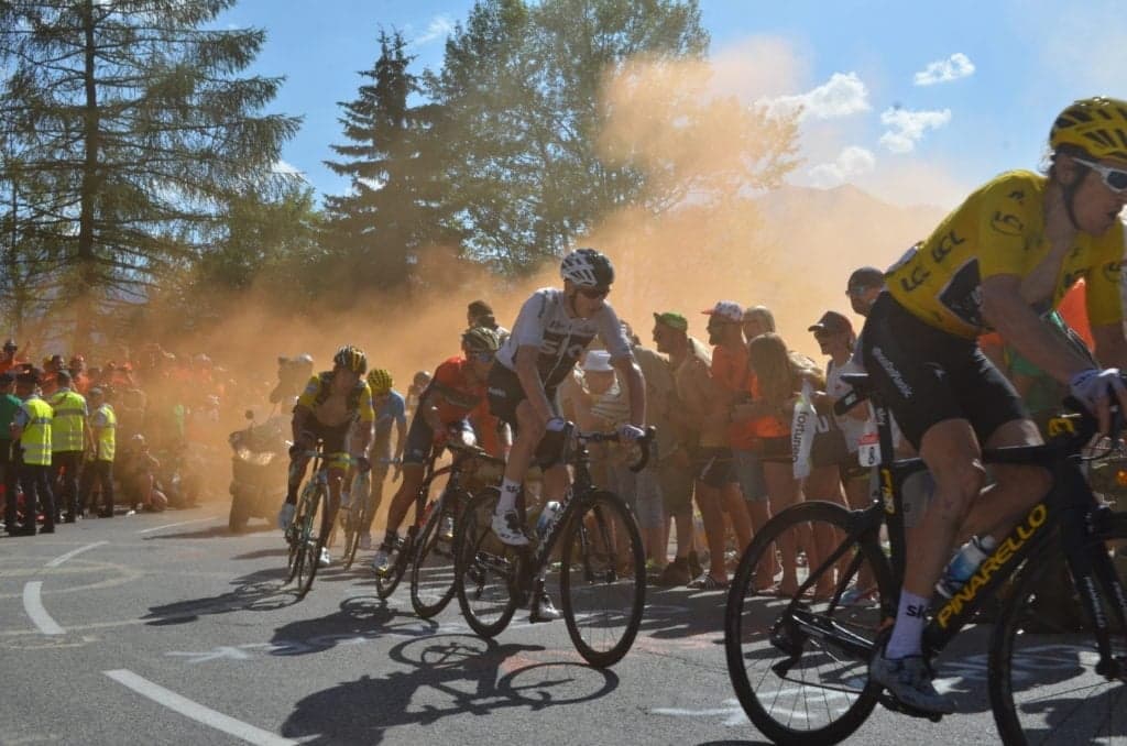 Cyclists in peloton with roadside crowd and orange smoke