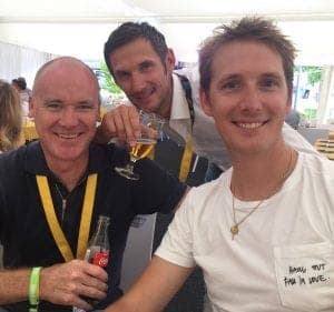 Three men posing indoors, one holding a drink