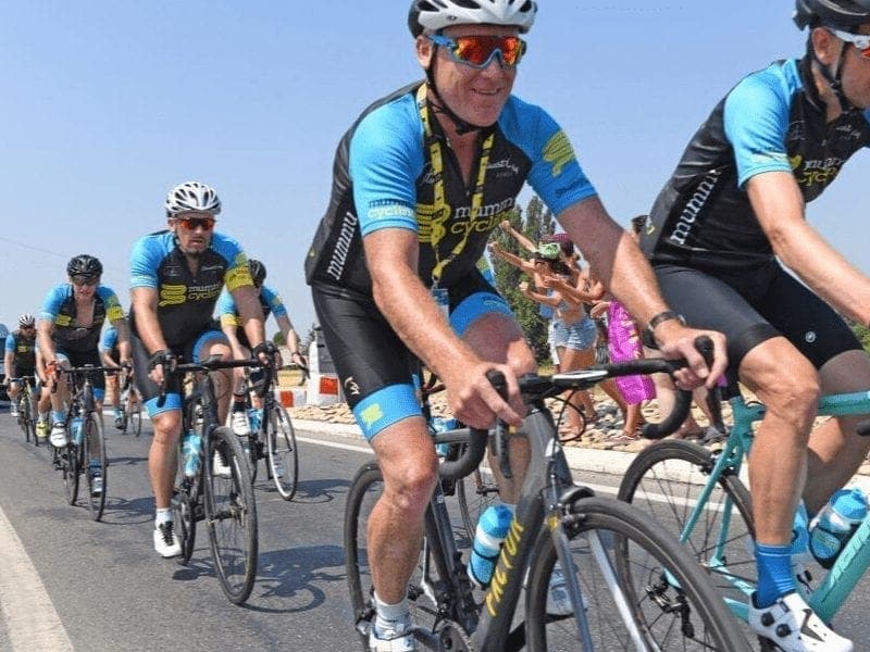 Group of cyclists in Mummu Cycling kit on a sunny road.