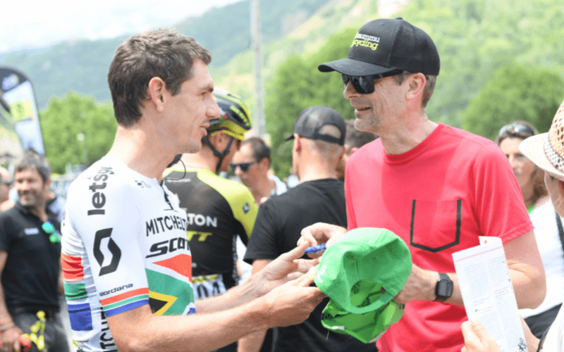 Cyclists in black and blue kits ride past a fan with face paint.