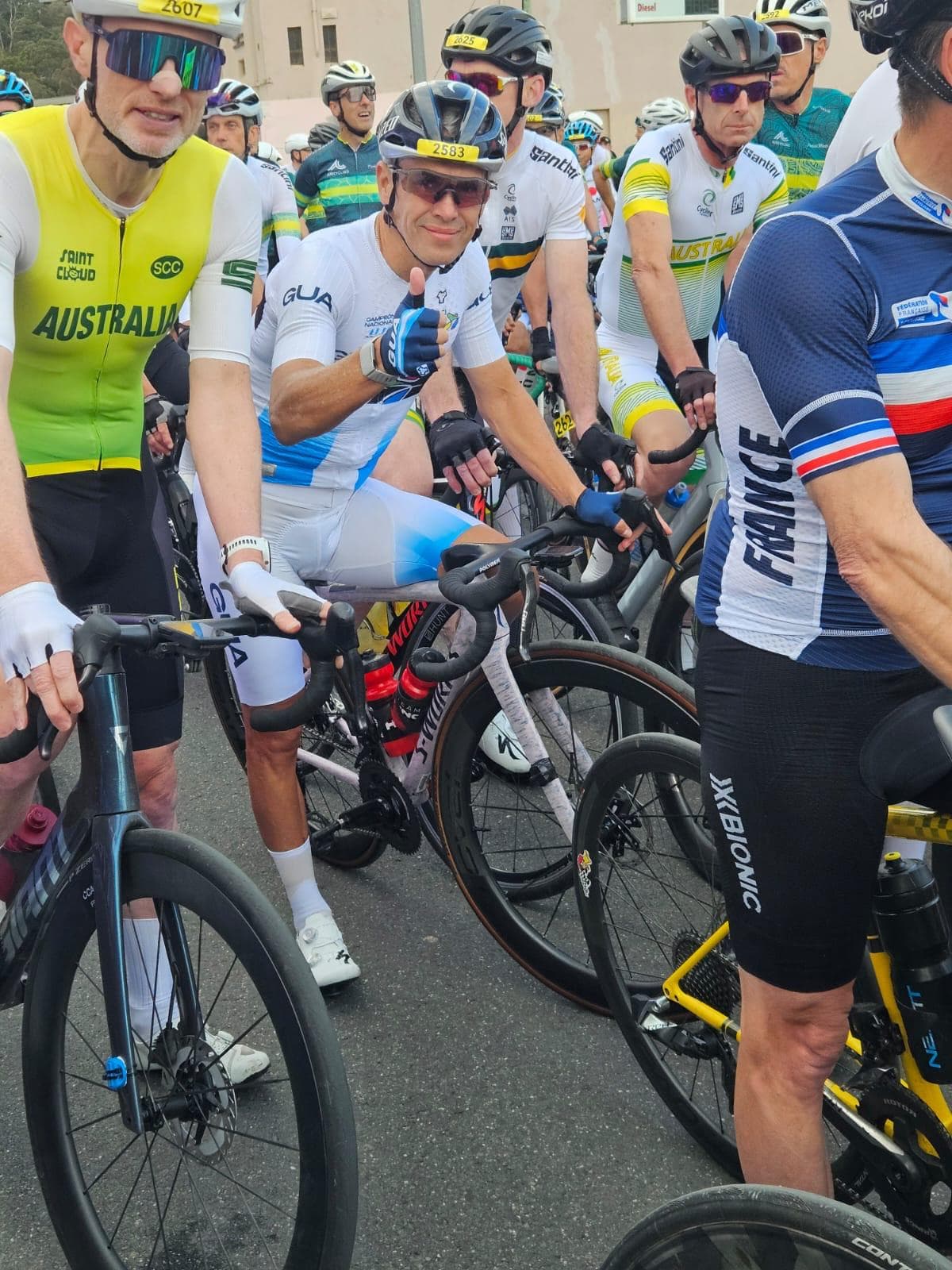Cyclists in Australian and French national champion jerseys, alongside a rider on a Specialized bike, lined up at a race start.