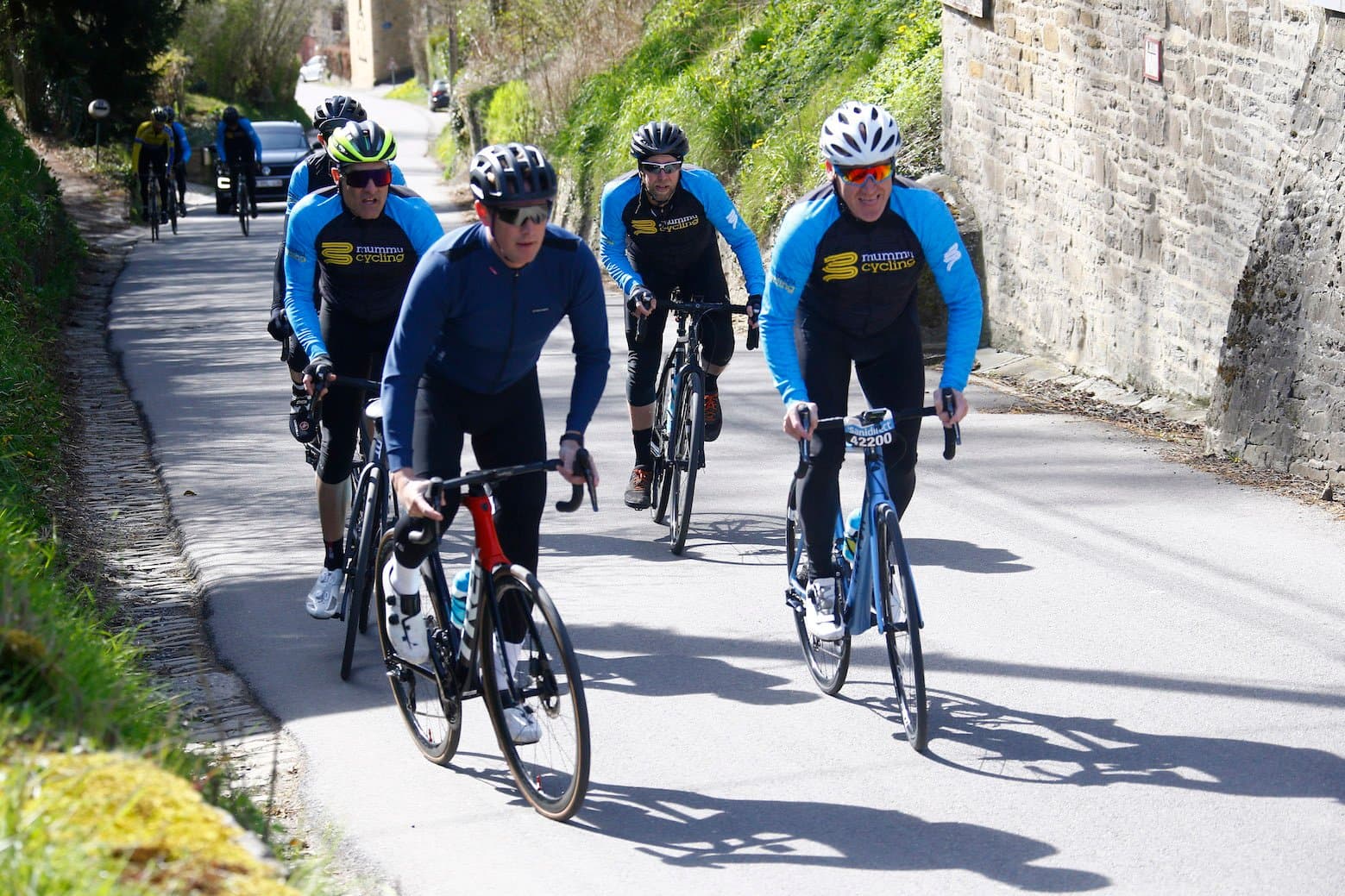 Group of cyclists in Mummu Cycling kit on a paved road.
