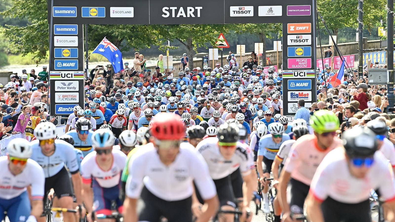 Cyclists massed at the start line of the Gran Fondo Road Race, 2023 UCI Cycling World Championships in Perth, Scotland, under the official start gantry.