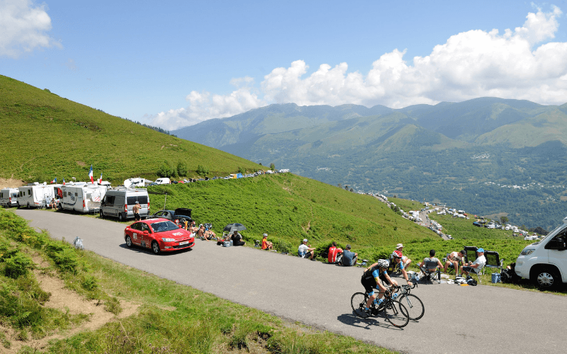 Cyclists climbing a mountain pass, spectators and support vehicles line the road.